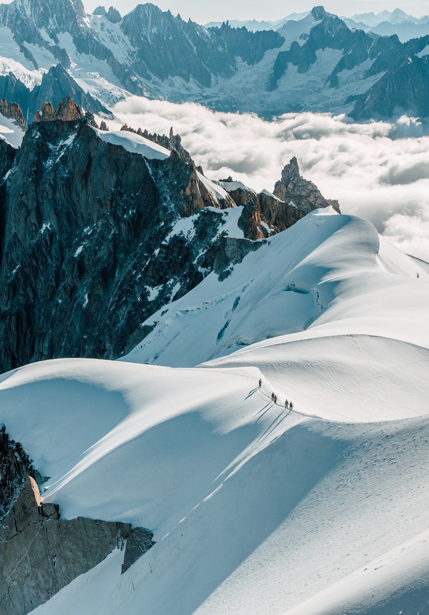 Una cordada cruza una cresta nevada muy por encima de un mar de nubes y agujas de granito