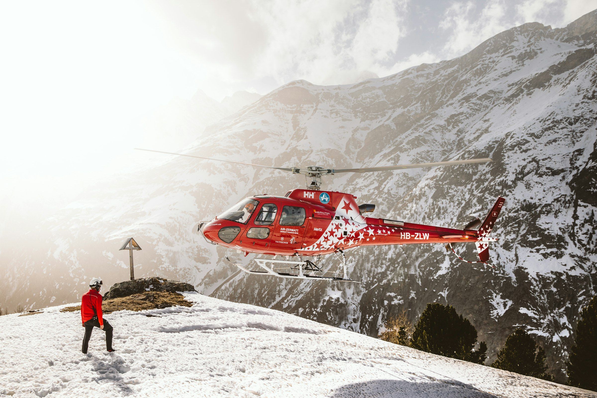 Un rescatador de montaña de rojo observa cómo un helicóptero de rescate despega de una ladera nevada